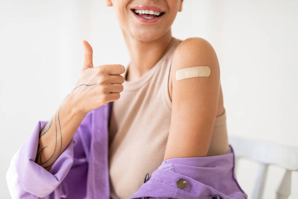 Successful covid-19 vaccination. Closeup view of lady gesturing thumb up and showing arm with adhesive bandage