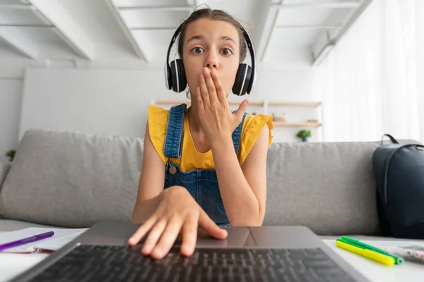 Chica sorprendida sentada en el escritorio, teniendo videollamada con auriculares — Foto de Stock