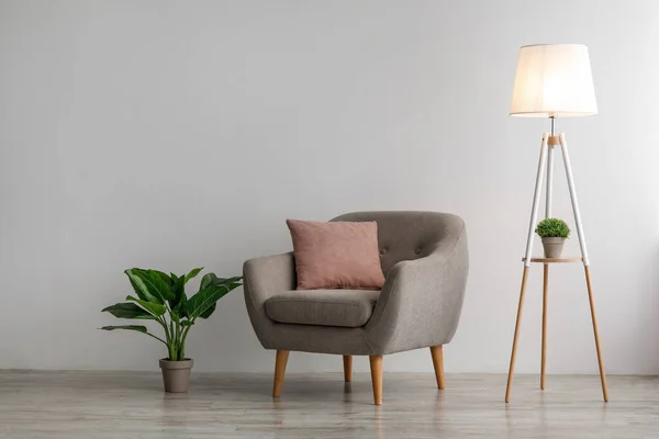Retro wygodny fotel z poduszką, świecącą lampą i rośliną doniczkową na podłodze na szarym tle ściany — Zdjęcie stockowe