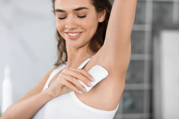 Glückliche Weibchen anwenden antitranspirant stick underarms im badezimmer indoor — Stockfoto