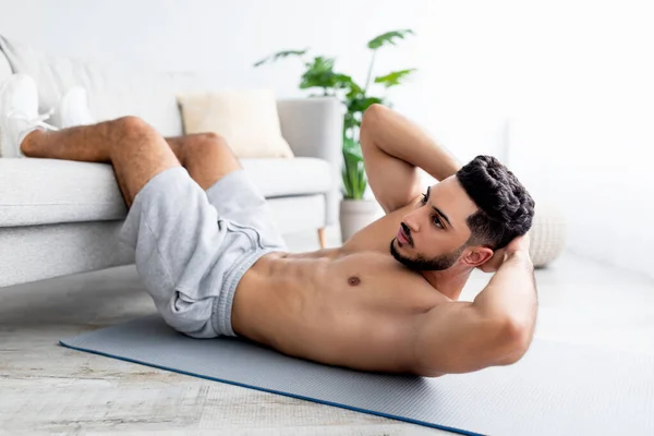 Hombre árabe joven con torso desnudo ejercitando los músculos abdominales en la esterilla de yoga en casa —  Fotos de Stock