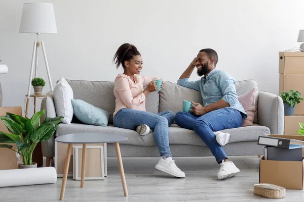 Feliz muito milenar família afro-americana sentar no sofá e beber café quente em novo apartamento com caixas de papelão — Fotografia de Stock