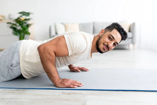 站在木板上的千年阿拉伯男子在瑜伽垫上摆姿势，在家里做力量练习 — 图库照片