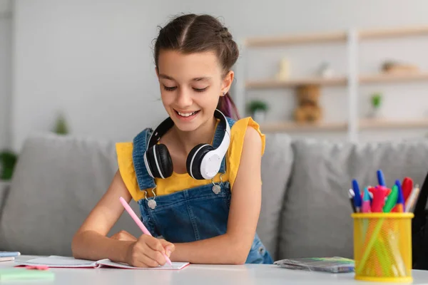 Lächelndes Mädchen sitzt am Tisch und schreibt in Notizbuch — Stockfoto