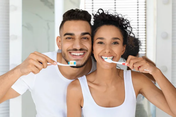 Cheerful Young Middle Eastern Couple Brushing Teeth Together And Smiling At Camera