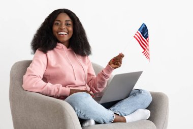 Dizüstü bilgisayarı olan siyah bir kadın ve koltukta Amerikan bayrağı.