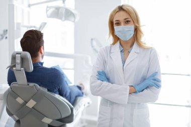 Diş kliniğinde poz veren koruyucu maskeli kadın diş hekimi.
