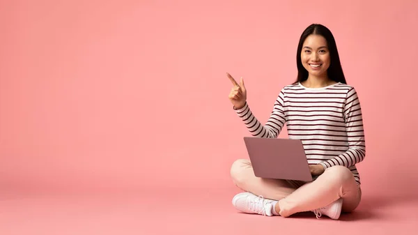 Mira esto. Sonriente joven asiática dama sentada con el ordenador portátil y señalando a un lado — Foto de Stock