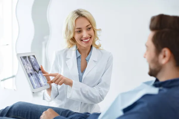 Vrouwelijke tandarts toont mannelijke patiënt röntgenfoto op digitale tablet — Stockfoto