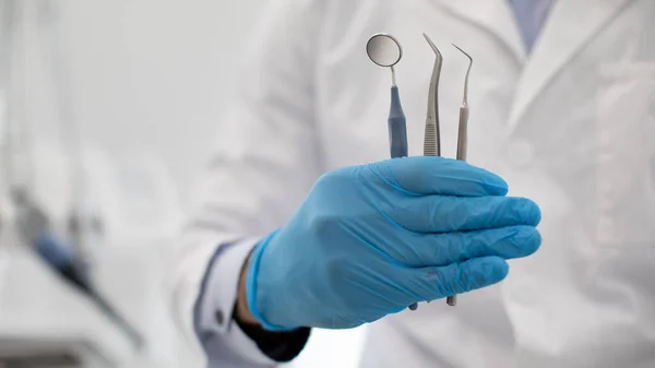 Médico dentista irreconocible en guante estéril azul sosteniendo herramientas dentales en la mano — Foto de Stock