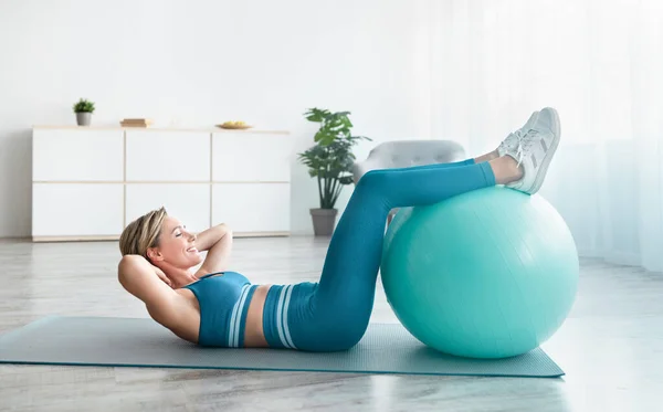 Mujer deportiva sonriente haciendo ejercicio con bola suiza en casa —  Fotos de Stock