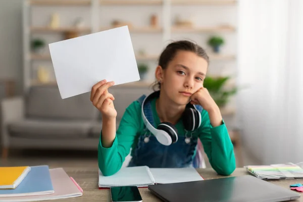 Втомлена шкільна дівчина сидить за столом тримає папір — стокове фото