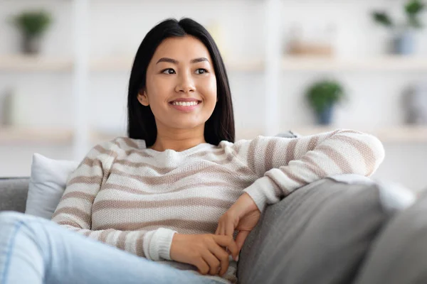 美丽的微笑的韩国女人在舒适的沙发上放松的画像 — 图库照片