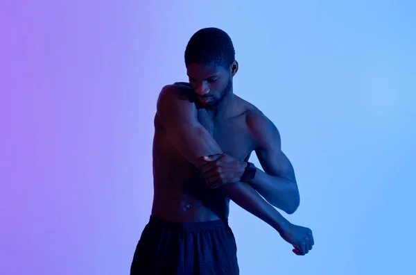 Homem negro atlético com tronco nu esticando o braço em iluminação de néon. Conceito de estilo de vida ativo — Fotografia de Stock