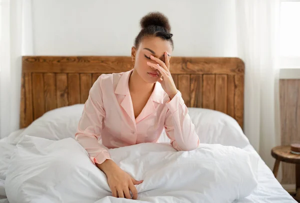 Zdenerwowana Afroamerykanka budzi się po ciężkim śnie, zmęczona lub bezsenna, siedzi na białym łóżku w sypialni, pusta przestrzeń — Zdjęcie stockowe