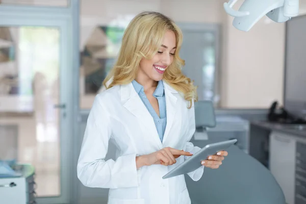 Attraktiv kvinnlig tandläkare med digital tablett ler medan du arbetar — Stockfoto