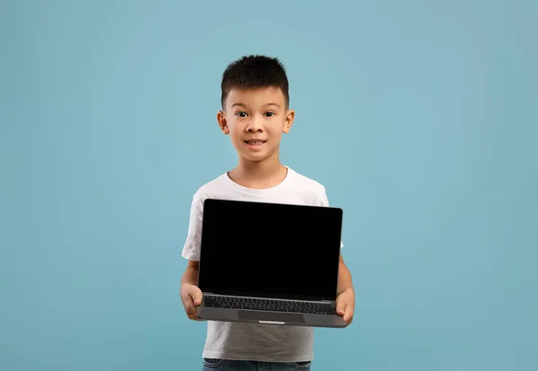 Маленький азиатский мальчик демонстрирует ноутбук с чистым черным экраном, макет — стоковое фото