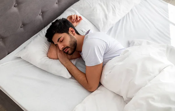 Hombre árabe joven dormido durmiendo, descansando tranquilamente en una cama cómoda, acostado con los ojos cerrados, espacio libre —  Fotos de Stock