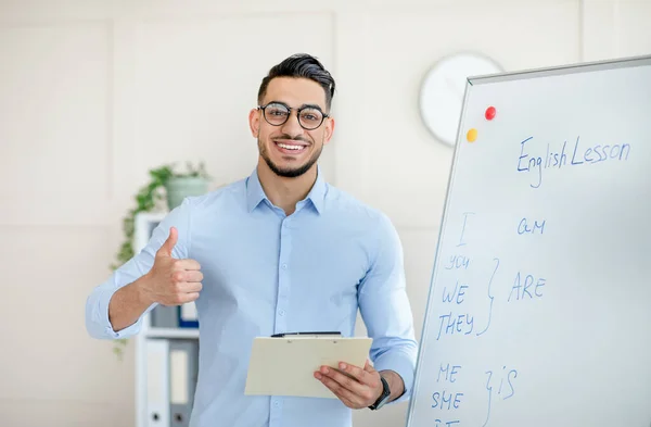 Profesor árabe positivo mostrando el pulgar hacia arriba cerca de pizarra, recomendando nueva escuela de idiomas extranjeros en línea — Foto de Stock