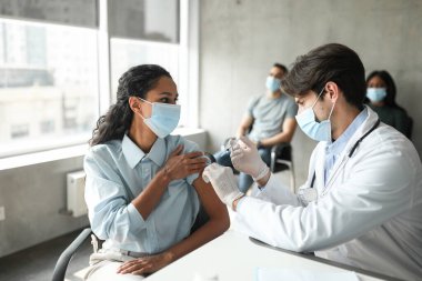 Kadın hasta aşı olurken yakışıklı doktora bakıyor.