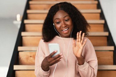 Afrikalı bir kadın akıllı telefondan evde otururken video görüşmesi yapıyor.