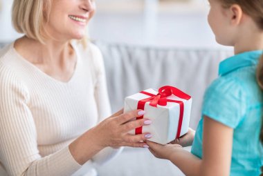 Büyük anneleri kutlayan küçük bir kız, paketlenmiş kutulu bir bayanı selamlayan bir kız.