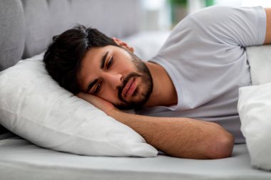 Üzgün Arap adam yatakta tek başına yatıyor, yalnızlık çekiyor ve sorunları düşünüyor. Erkek stresi ve depresyon kavramı