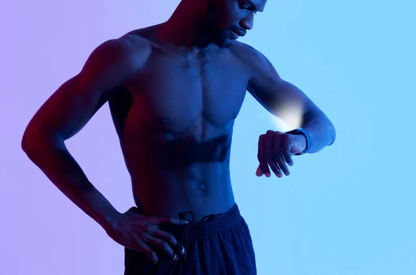 Ausgeschnittene Ansicht eines hübschen jungen Schwarzen mit nacktem Oberkörper, der Fitness-Tracker im Neonlicht überprüft — Stockfoto