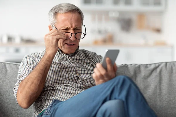 Hombre mayor entrecerrando los ojos Lectura Mensaje Usando anteojos en casa — Foto de Stock