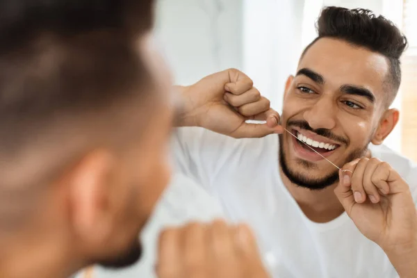 Higiene oral. guapo árabe chico usando dental floss mientras buscando en espejo — Foto de Stock