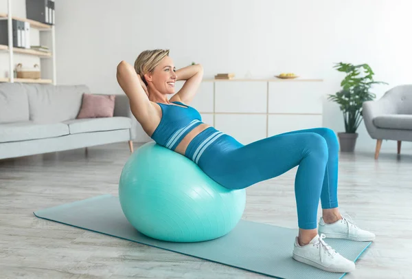 Mujer Deportiva Sonriente haciendo ejercicio apoyándose en la pelota de fitness en casa —  Fotos de Stock