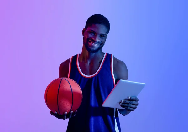 Portrait of professional player with basketball using tablet computer in neon lighting. Konsep permainan olahraga — Stok Foto