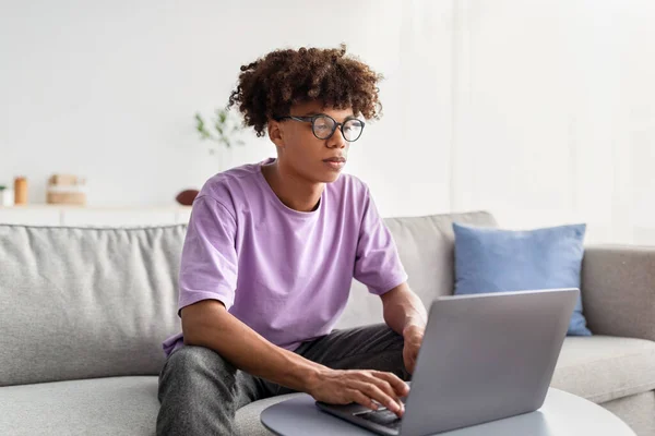 Poważny czarny nastolatek za pomocą laptopa do badań online, odrabianie prac domowych, przygotowuje się do testu w domu — Zdjęcie stockowe