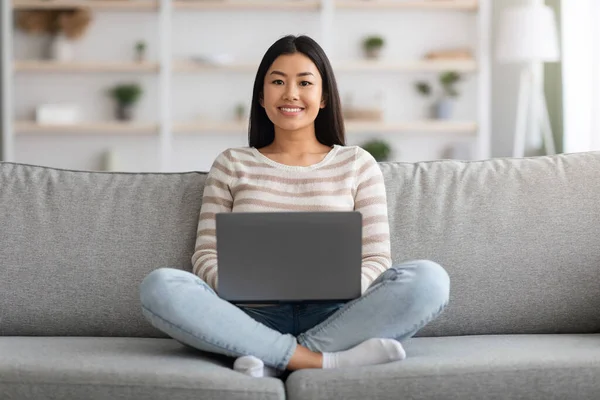 Fernarbeit. Junge Asiatin mit Laptop auf Couch zu Hause — Stockfoto