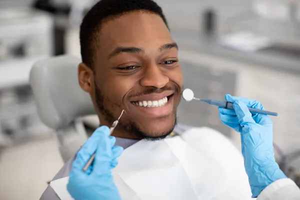 Serviços Odontológicos. Jovem preto masculino paciente sentado na cadeira na clínica dentária — Fotografia de Stock