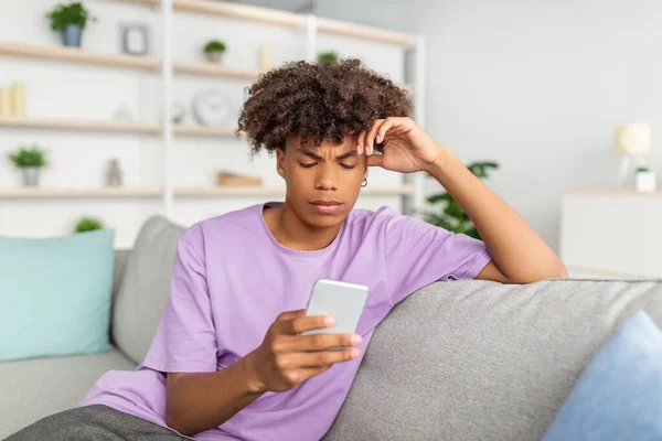 Funky preto adolescente cara com telefone celular estudando on-line, mensagens com amigo, postando em rede social de casa — Fotografia de Stock