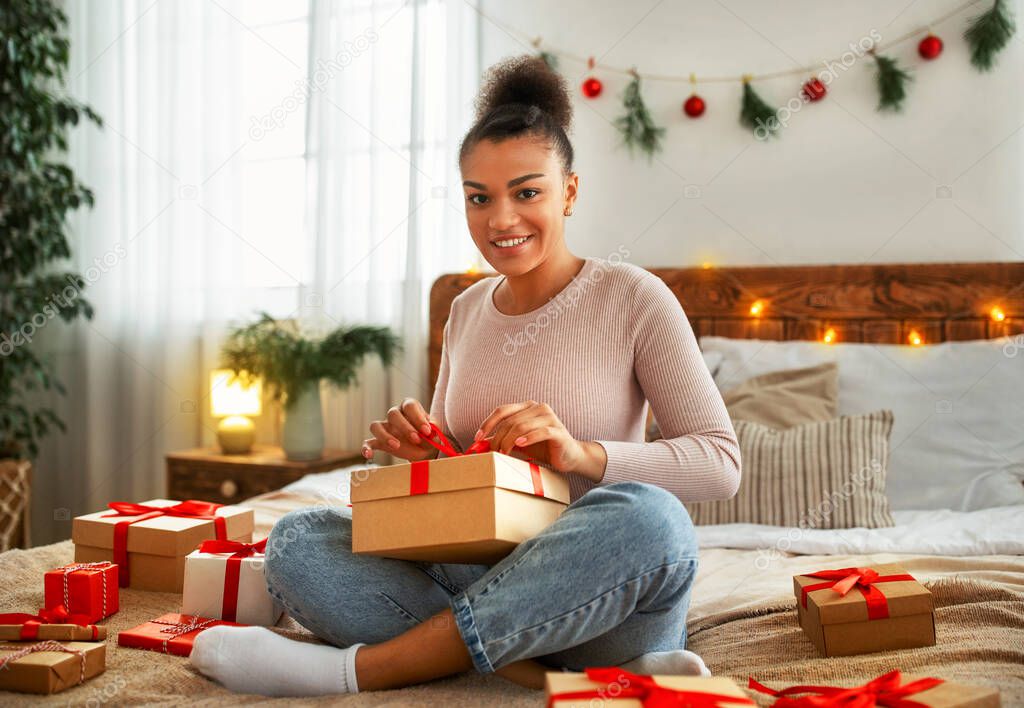 Christmas and new year celebration. Happy african american lady opening xmas present and smiling at camera