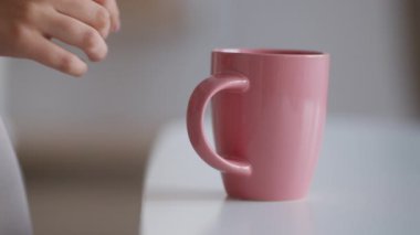 Tanımlanamayan beyaz bir kadının evdeki masadan sıcak çayla pembe fincanı alıp yavaş çekimde, serbest bırakması.