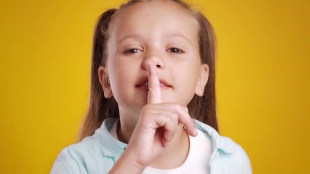 Håll tyst. Rolig liten flicka som visar shh tecken, hålla fingret på läppar och titta på kameran, orange studio bakgrund — Stockvideo