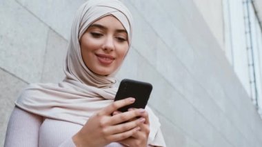 İnternet iletişimi. Açık havada akıllı telefondan tesettürlü tesettürlü Müslüman bir kadının portresinin altında.