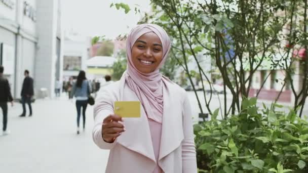 Бизнес и финансы. Счастливая африканская американская мусульманская деловая женщина в хиджабе, показывающая кредитку и улыбающаяся — стоковое видео