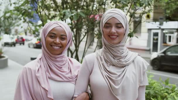 Odkryty portret dwóch wielonarodowych muzułmańskich przyjaciółek w hidżabach, pozujących na świeżym powietrzu i uśmiechających się do kamery — Wideo stockowe