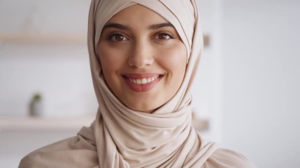 Vacker lugn mellanösternmuslimsk kvinna bär ljus traditionell hijab tittar och ler mot kameran, poserar hemma — Stockvideo