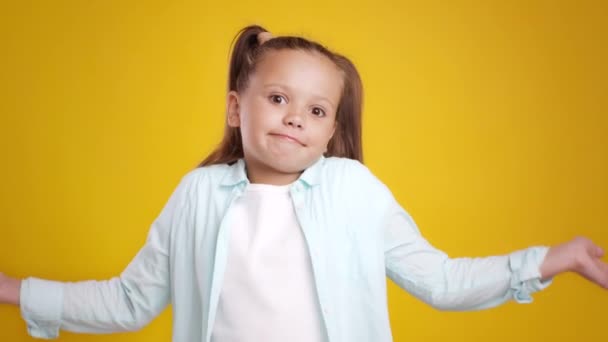 哎呀，这不是我。可爱而不确定的小女孩耸了耸肩，伸出双手，橙色背景 — 图库视频影像