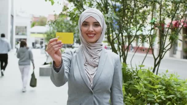 Independência financeira das mulheres muçulmanas. Senhora de negócios do Oriente Médio confiante mostrando cartão de crédito para câmera e sorrindo — Vídeo de Stock