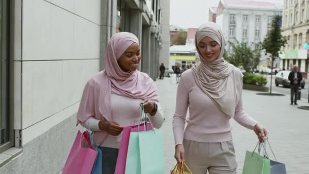 Zwarte vrijdag verkoop. Twee vrolijke moslimvrouwen lopen met veel boodschappentassen en lachen, genieten van herfstshoppen — Stockvideo