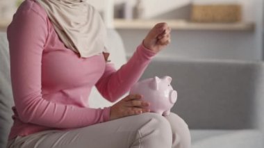 Kişisel tasarruf kavramı. Geleneksel türbanlı tanınmayan Müslüman kadın domuz kumbarasına bozuk para koyuyor.