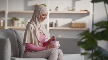 Para tasarrufu konsepti. Huzurlu orta doğulu kadın evdeki domuz kumbarasına bozuk para koyuyor.