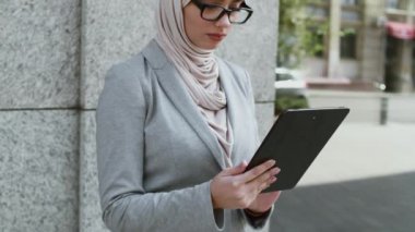 Kablosuz teknolojiler. Genç Müslüman iş kadını tesettür ve gözlük takıyor dışarıda dijital tablet üzerinde çalışıyor.