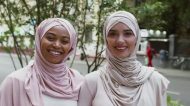 Geleneksel türbanlı Afrikalı Amerikalı ve ortadoğulu Müslüman kadınlar kameraya gülümsüyor, açık havada birbirlerine bağlanıyorlar.